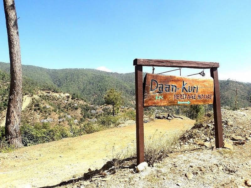 Wooden signboard for Daankudi Heritage House on a scenic mountain road