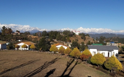 Resort grounds with white cottages, yellow-leaved trees, and distant snow mountains.