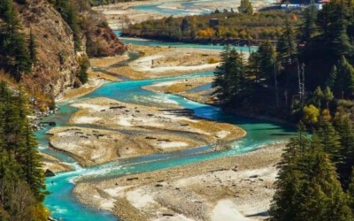 A winding turquoise river flowing through a wide riverbed surrounded by trees in a mountain valley